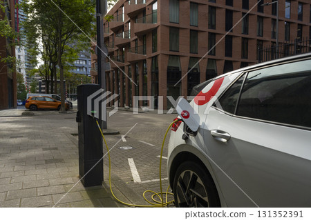 A white electric vehicle charging at a public charging station on a city street. 131352391