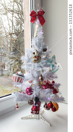 Cozy holiday details with baubles and tinsel on a white artificial Christmas tree standing on the window sill. Cozy holiday details with baubles and tinsel on a white artificial Christmas tree standing on the window sill. 131352618