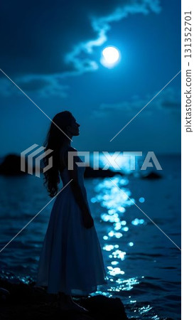 Woman in white dress stands by the ocean under a bright moonlight at night, creating a serene atmosphere 131352701