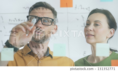 Professional businesspeople collaborating, reviewing data on transparent whiteboard, developing strategic corporate solutions in modern collaborative workspace. Business people concept Professional businesspeople collaborating, reviewing data on transparent whiteboard, developing strategic corporate solutions in modern collaborative workspace. Business people concept 131352771