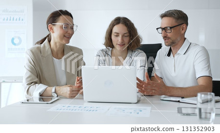Professional team reviewing project data on laptop, working together in modern office environment, collaborating with focused corporate energy Professional team reviewing project data on laptop, working together in modern office environment, collaborating with focused corporate energy 131352903