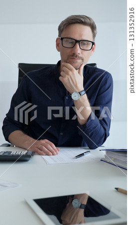 Businessman sitting at a sleek desk, working on a laptop and thinking in a bright, modern office filled with natural light. Business people concept Businessman sitting at a sleek desk, working on a laptop and thinking in a bright, modern office filled with natural light. Business people concept 131352916