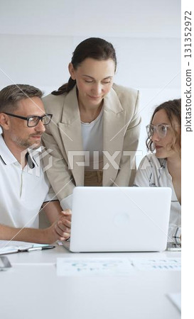 Business people working together, reviewing data on laptop screen, sharing insights during collaborative office meeting, emphasizing professional teamwork 131352972