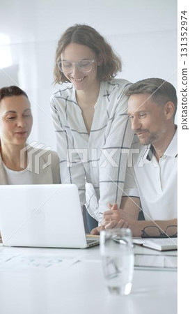 Professional team reviewing project data on laptop, working together in modern office environment, collaborating with focused corporate energy 131352974