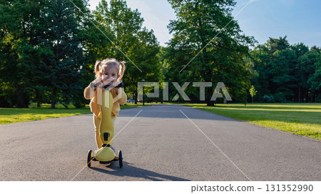 Little girl scooter. Toddler riding yellow scooter. Park road summer play. Little girl scooter. Toddler riding yellow scooter. Park road summer play. 131352990