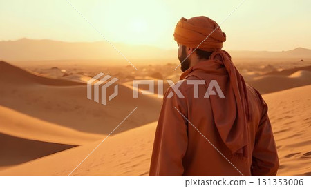 Man in traditional attire gazes at sunset over vast desert landscape with rolling sand dunes during golden hour 131353006