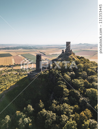 Hazmburk castle ruins rise above the lush landscape of Czechia, showcasing medieval architecture. Situated in the Central Bohemian Uplands, the site offers breathtaking views of surrounding fields. 131353445