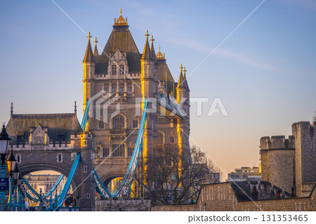 Morning light casts a warm glow on Tower Bridge as it spans the River Thames. The iconic structure stands tall against the clear sky, reflecting London's historic charm and beauty. 131353465