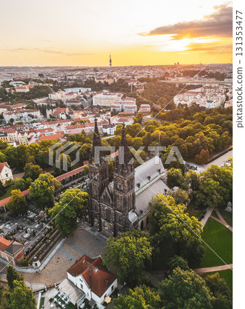 Morning light bathes Vysehrad Basilica of St. Peter and St. Paul in a golden glow, highlighting its gothic architecture amidst the lush scenery of Prague. A tranquil start to the day unfolds. 131353477