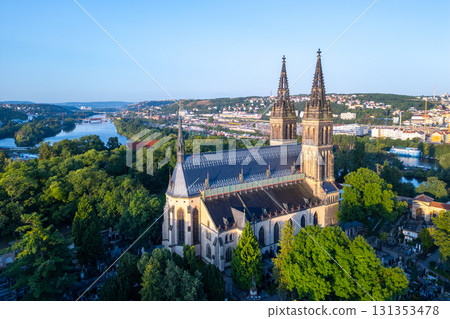 Golden sunlight bathes the Basilica of St. Peter and St. Paul in Prague during a tranquil morning. Surrounded by lush greenery, the historic structure stands majestically against the skyline. 131353478