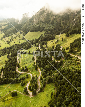 Aerial view captures serpentine roads meandering through the vibrant green hills of the Alps, showcasing nature's beauty on an adventurous journey through the mountains. 131353481