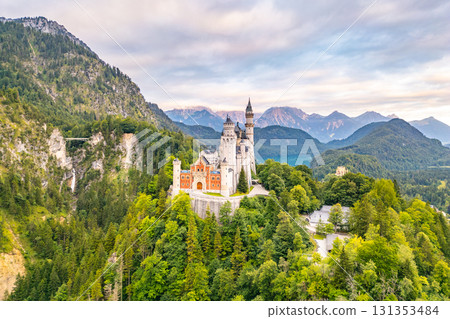 Perched on a hilltop, Neuschwanstein Castle stands gracefully against the backdrop of the Bavarian Alps, surrounded by lush forests and breathtaking mountains. A true fairytale structure. Perched on a hilltop, Neuschwanstein Castle stands gracefully against the backdrop of the Bavarian Alps, surrounded by lush forests and breathtaking mountains. A true fairytale structure. 131353484