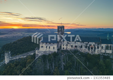 Bezdez Castle stands majestically on a hilltop, with its ancient towers silhouetted against a vibrant sunset. The evening light highlights the castle's medieval architecture and surrounding landscape. Bezdez Castle stands majestically on a hilltop, with its ancient towers silhouetted against a vibrant sunset. The evening light highlights the castle's medieval architecture and surrounding landscape. 131353485