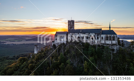 Bezdez Castle, a medieval ruin perched on a hill, offers a stunning aerial view as the sun sets in the evening sky. The silhouette of the tower contrasts beautifully against vibrant colors of dusk. Bezdez Castle, a medieval ruin perched on a hill, offers a stunning aerial view as the sun sets in the evening sky. The silhouette of the tower contrasts beautifully against vibrant colors of dusk. 131353486