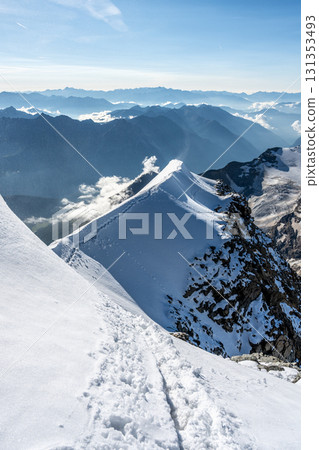 Hikers navigate the exposed summit ridge of Piz Palu, surrounded by snow and steep cliffs. The Bernina Range's breathtaking vistas stretch across the Swiss Alps on a clear summer day. Hikers navigate the exposed summit ridge of Piz Palu, surrounded by snow and steep cliffs. The Bernina Range's breathtaking vistas stretch across the Swiss Alps on a clear summer day. 131353493