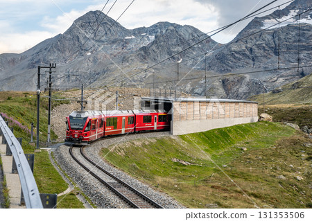 The Bernina railway winds through the breathtaking Swiss Alps near Bernina Pass, showcasing stunning mountain views and lush greenery in Graubunden. 131353506