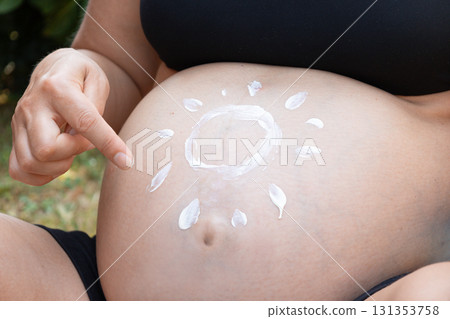 Expecting woman applies sunscreen in the shape of a sun on her bare belly, symbolizing pregnancy care, skin protection, and maternal love under summer sunlight Expecting woman applies sunscreen in the shape of a sun on her bare belly, symbolizing pregnancy care, skin protection, and maternal love under summer sunlight 131353758