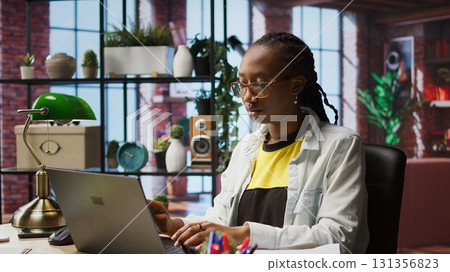 Teleworker analyzing data on laptop at desk and looking over paperwork, compiling analytical reports. Remote employee checking documents, using notebook to upload company information online, camera A Teleworker analyzing data on laptop at desk and looking over paperwork, compiling analytical reports. Remote employee checking documents, using notebook to upload company information online, camera A 131356823