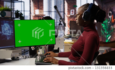 African american woman uses mockup PC in AI tech company providing software development services. Startup IT expert uses AI to streamline coding process on green screen PC African american woman uses mockup PC in AI tech company providing software development services. Startup IT expert uses AI to streamline coding process on green screen PC 131356833