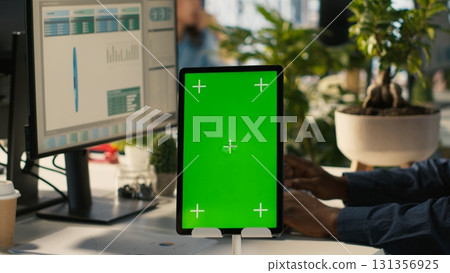 Close up of green screen tablet in front of employee checking progress done on project. Chroma key device next to office clerks reading data statistics on PC screen, camera A 131356925