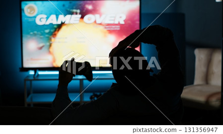 Male gamer getting frustrated with his failure and lost gaming competition, angry young man losing video games challenge online with friends. Modern smart tv setup for game night at home. Camera B. Male gamer getting frustrated with his failure and lost gaming competition, angry young man losing video games challenge online with friends. Modern smart tv setup for game night at home. Camera B. 131356947