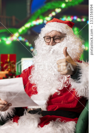 Pleased Santa Claus gives thumbs up after reading letters from children on nice list. Upbeat Father Christmas looking at wish list, doing positive hand gesture, satisfied with kids who did good deeds Pleased Santa Claus gives thumbs up after reading letters from children on nice list. Upbeat Father Christmas looking at wish list, doing positive hand gesture, satisfied with kids who did good deeds 131356994