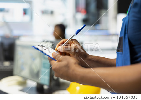 Black photovoltaics facility engineer monitoring system performance on clipboard. Solar panels manufacturing plant supervisor pleased by high production, industrial quality control. Black photovoltaics facility engineer monitoring system performance on clipboard. Solar panels manufacturing plant supervisor pleased by high production, industrial quality control. 131357035