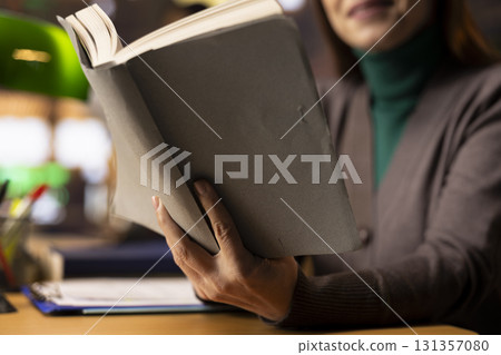 Adult female scholar reading a book in a study area at the library, reviewing academic materials and looking for citations sources. Mature student determined to graduate college. Close up. Adult female scholar reading a book in a study area at the library, reviewing academic materials and looking for citations sources. Mature student determined to graduate college. Close up. 131357080