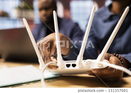 African american woman rebooting their WI FI router modem by moving cables, hoping to solve their ongoing internet issues and speed. Stable wireless connection for freelance tasks. Close up. 131357081
