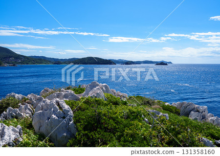和歌山白崎海岸,石灰岩巨石遍布的海岸線,白色的岩石散佈在綠色的山丘之間,遠處的海對面是山脈 和歌山白崎海岸,石灰岩巨石遍布的海岸線,白色的岩石散佈在綠色的山丘之間,遠處的海對面是山脈 131358160