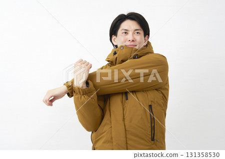 Man wearing down jacket stretching arms white background 131358530