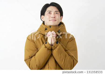 A man wearing a down jacket prays on a white background A man wearing a down jacket prays on a white background 131358533
