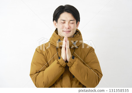 一名身穿羽絨外套的男子雙手合十在白色背景上祈禱 131358535