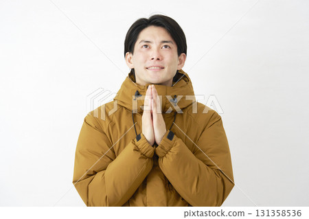 一名身穿羽絨外套的男子雙手合十在白色背景上祈禱 131358536