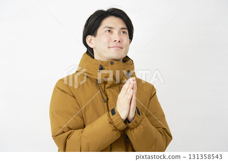 A man wearing a down jacket praying with his hands together on a white background A man wearing a down jacket praying with his hands together on a white background 131358543
