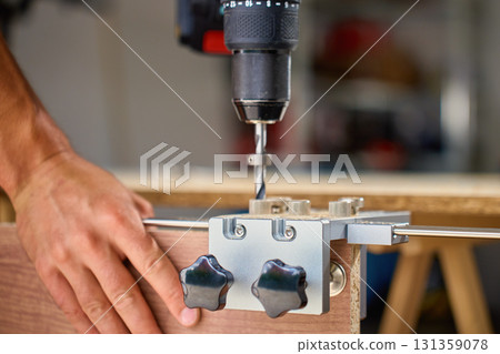 Carpenter drilling wooden panel using jig tool for precise holes 131359078