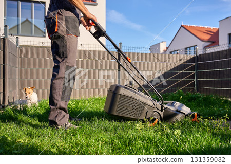 Man mowing grass in backyard with dog 131359082