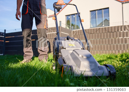 Man mowing lawn with electric mower in backyard 131359083