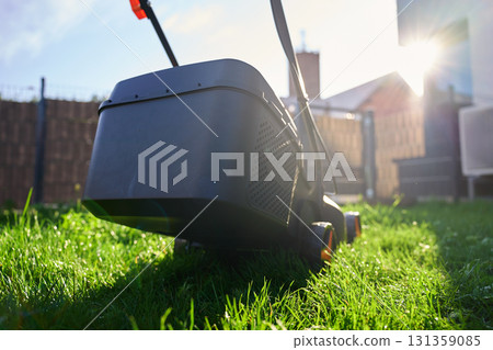 Electric lawn mower cutting green grass in backyard 131359085