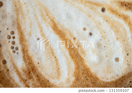 Full frame shot of the surface of hot latte coffee. A latte is a coffee drink made with espresso and steamed milk. Full frame shot of the surface of hot latte coffee. A latte is a coffee drink made with espresso and steamed milk. 131359107