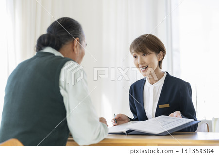 A businesswoman talking to a senior man while showing him documents A businesswoman talking to a senior man while showing him documents 131359384