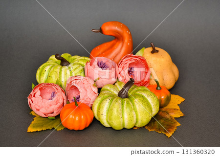 Autumn arrangement with pumpkins, autumn leaves and pink flowers on a gray background 131360320
