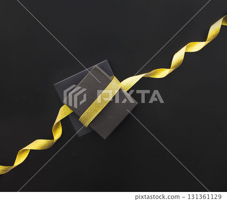 Two black gift boxes with a shiny yellow ribbon on a black background. Ideal for Black Friday sale promotions and holiday shopping themes. 131361129