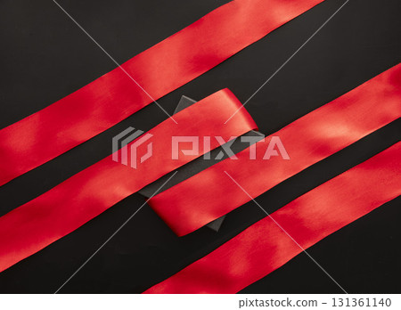 Red satin ribbons arranged on a black background, ideal for gift wrapping during Black Friday sales. The vibrant color contrasts with the dark surface. 131361140
