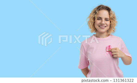 Smiling woman shows pink ribbon on her shirt for cancer awareness Smiling woman shows pink ribbon on her shirt for cancer awareness 131361322