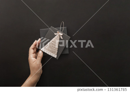 A hand holds a decorative Christmas card with a tree design. The background is dark, emphasizing the card's details. Ideal for Black Friday sale promotions. 131361785