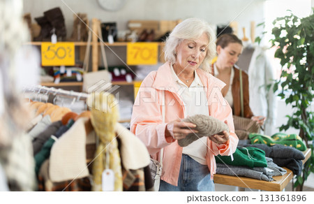Senior woman customer examine and choose hat. Other buyer in background, crowded shop Senior woman customer examine and choose hat. Other buyer in background, crowded shop 131361896