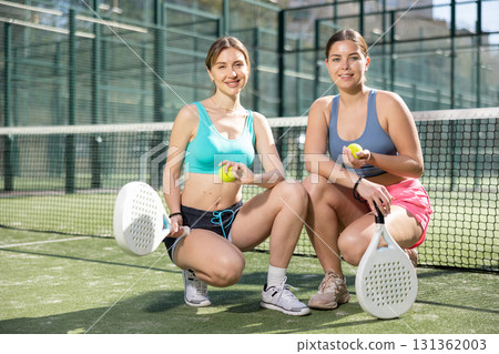 Two young sporty girls getting ready for padel game in court on sunny day 131362003