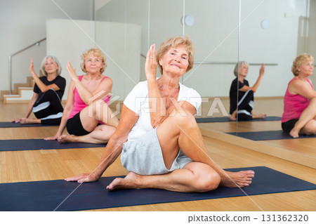 Smiling senior woman sitting in twisting asana Matsyendrasana Smiling senior woman sitting in twisting asana Matsyendrasana 131362320