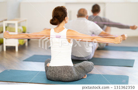 Group of men and women exercising with pilates loop back view Group of men and women exercising with pilates loop back view 131362350